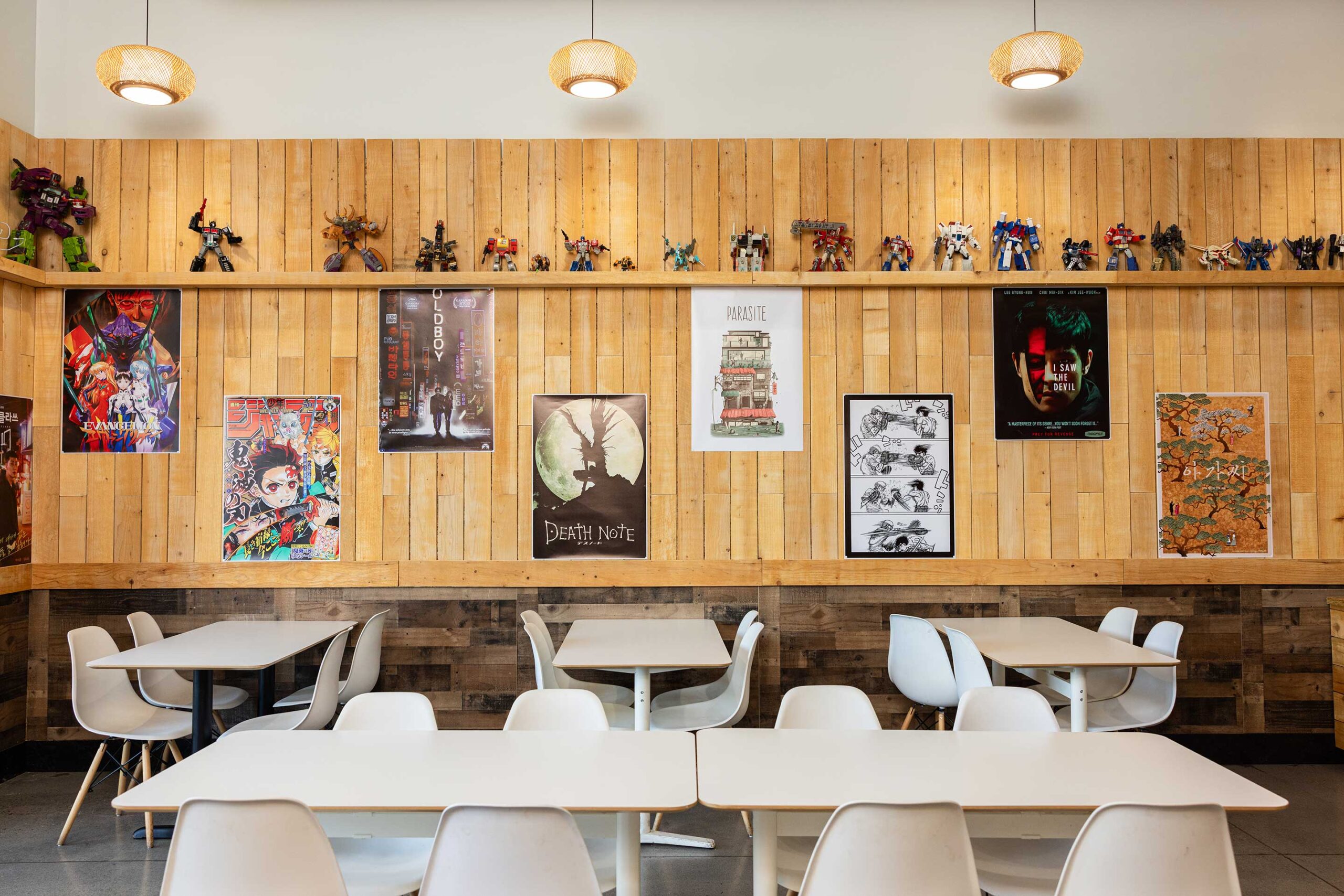 Interior shot of the Kim Jong Grillin restaurant in Happy Valley, Oregon, featuring modern white tables and chairs and Korean movie posters on the walls along with a collection of anime figurines