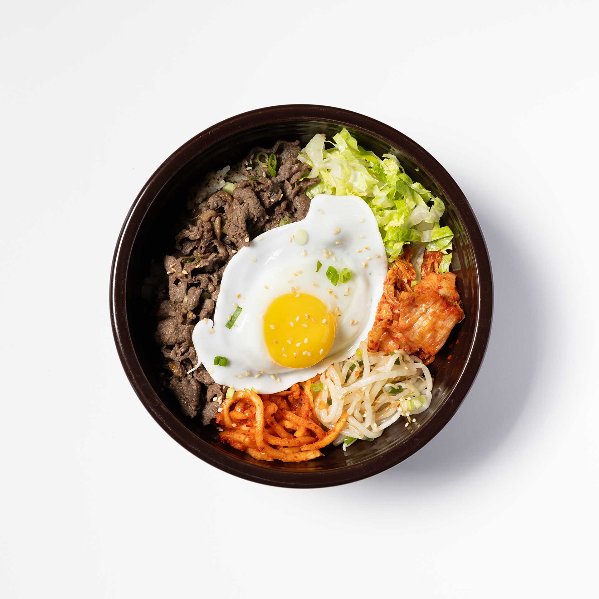 overhead shot of a black bowl containing traditional korean bulgogi bibimbap topped with kimchi, sprouts, and a fried egg