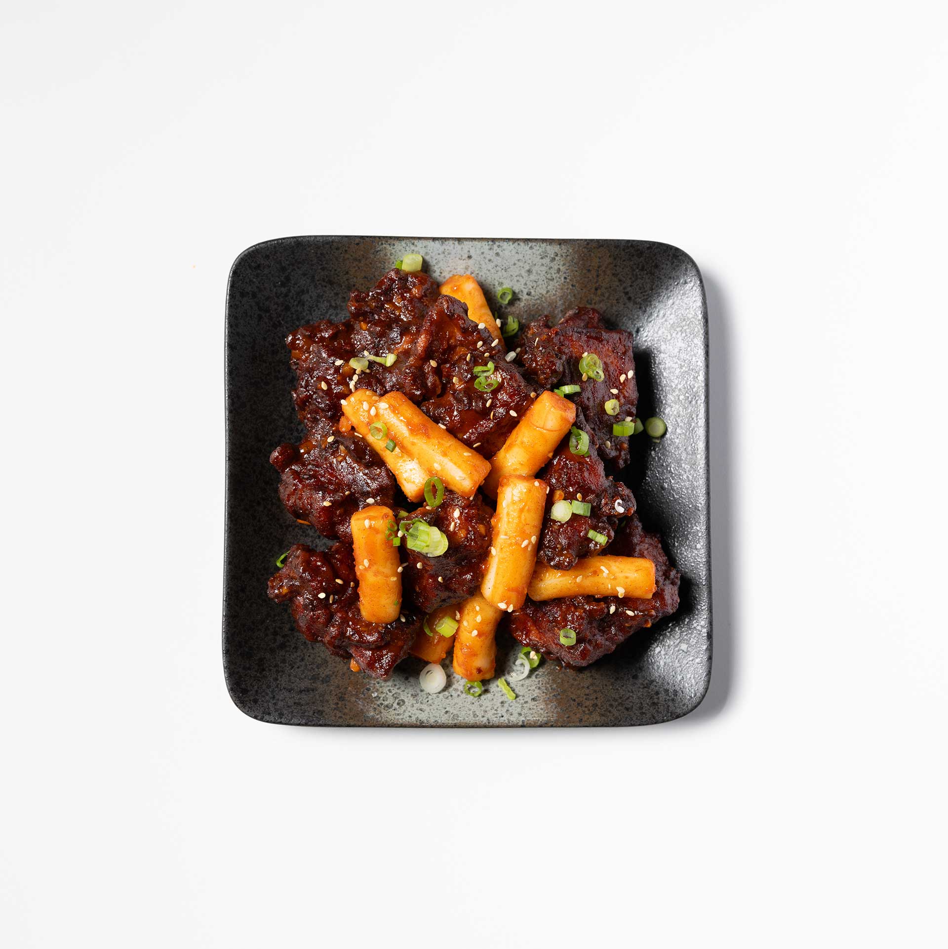 small black square plate containing fried chicken and rice cakes