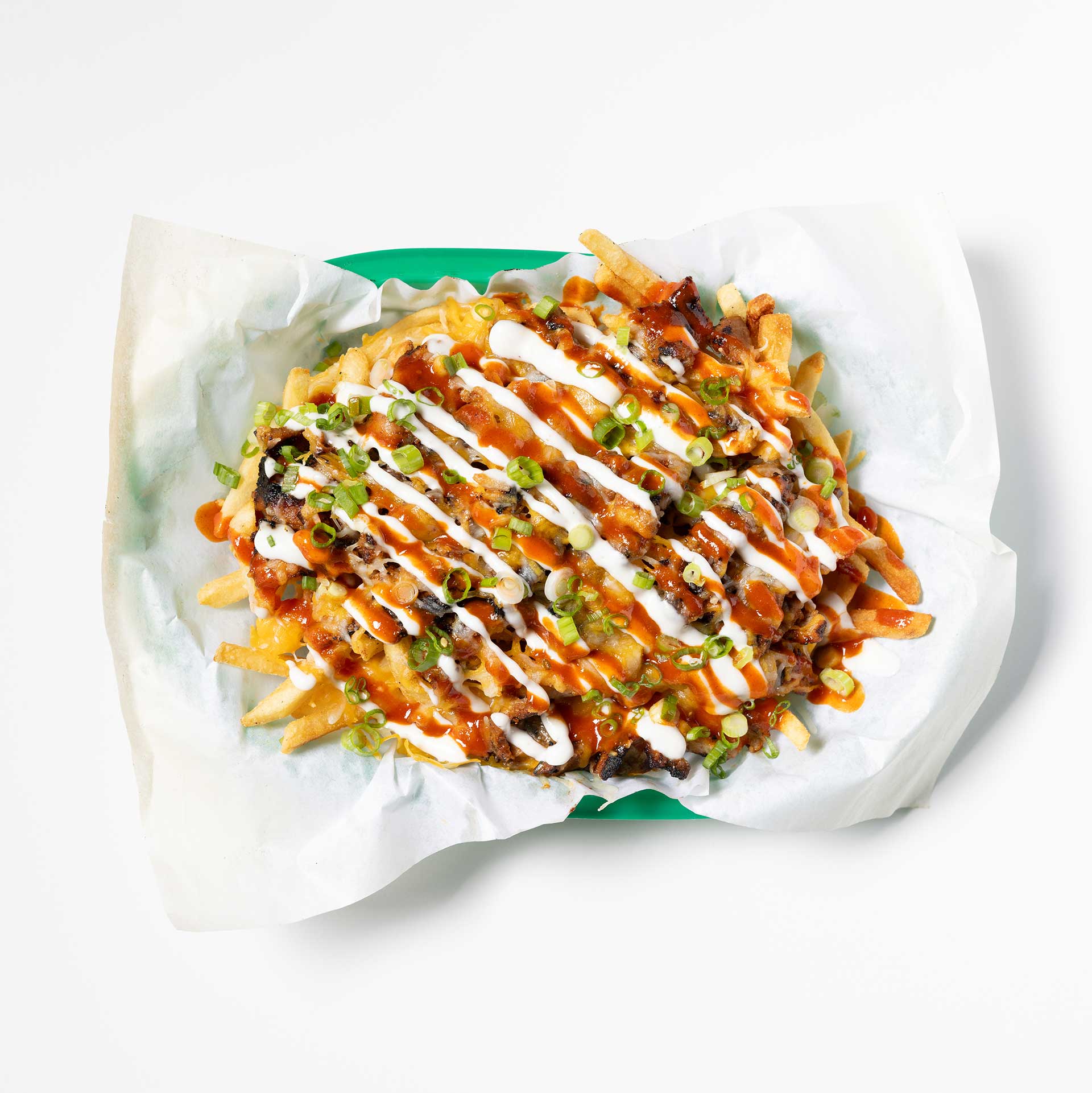 a green basket with wax paper holding a plate of french fries smothered in meats and a variety of sauces