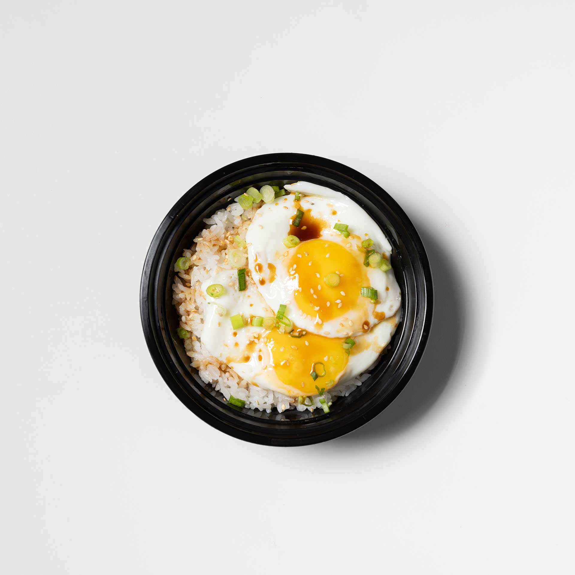 small black bowl containing fried eggs and scallions a top a bed of rice and soy sauce